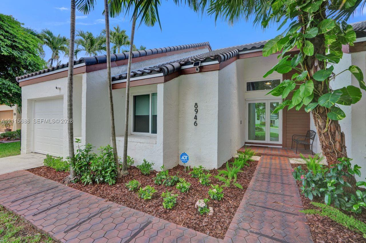 Stucco exterior featuring a dual-pitch tile roof, paver walkway, single-car garage, and glass-paneled entry door with transom window