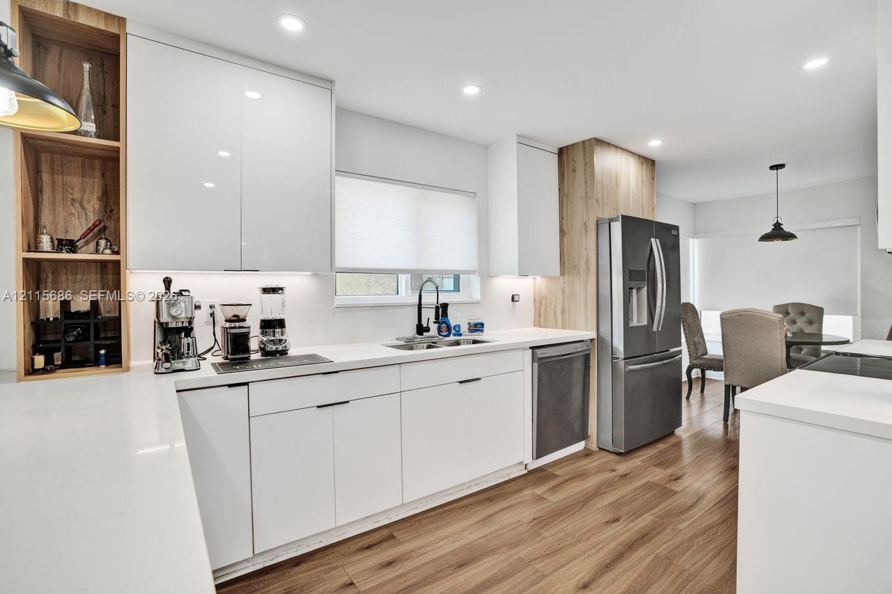 Kitchen featuring white flat-panel cabinetry, light-toned wood-finish vertical accents, solid-surface countertops, recessed lighting, and wood-finish flooring