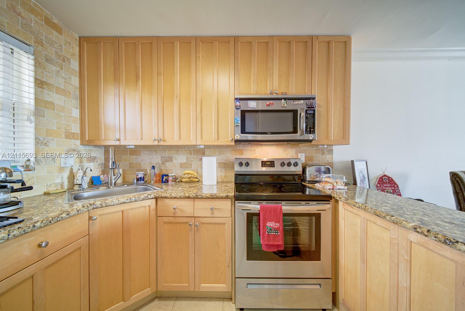 Kitchen featuring natural wood cabinetry, stone-surface countertops, textured stone backsplash, and stainless steel appliances including a range and over-the-range microwave