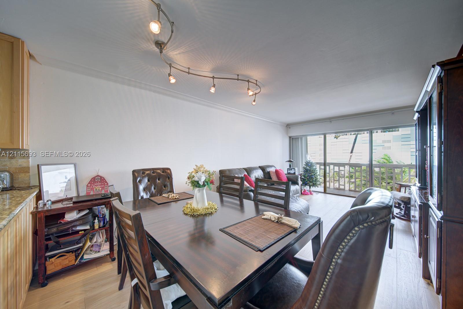 Multi-light adjustable track lighting, wood-finish flooring, and floor-to-ceiling glass sliding doors opening to an outdoor balcony