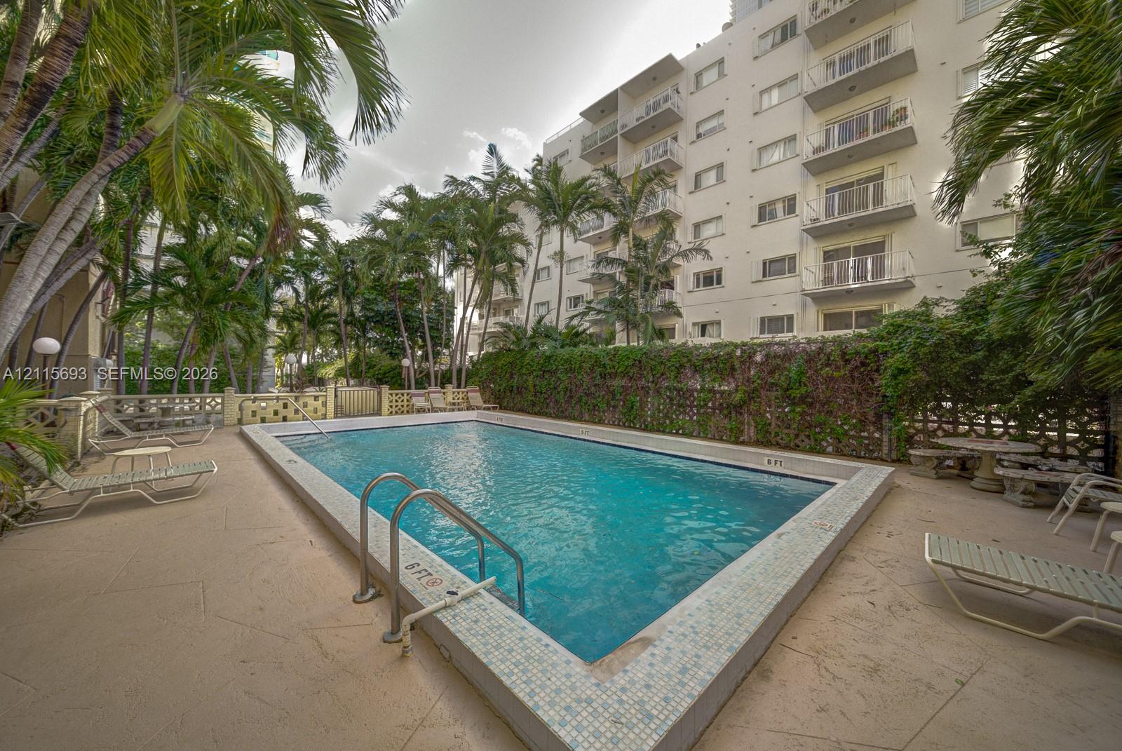 In-ground rectangular swimming pool with tile-edge coping, surrounding stone-finish decking, and privacy fencing complemented by mature palms and landscaping