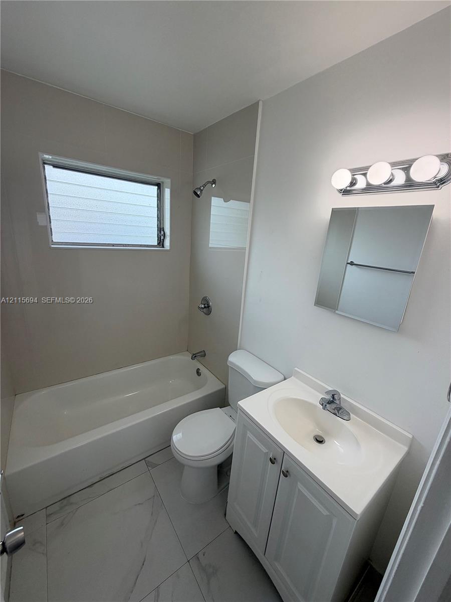 Bathroom featuring a shower-tub combination, vanity with an integrated sink, polished chrome fixtures, wall-mounted mirror, and large-format tile flooring