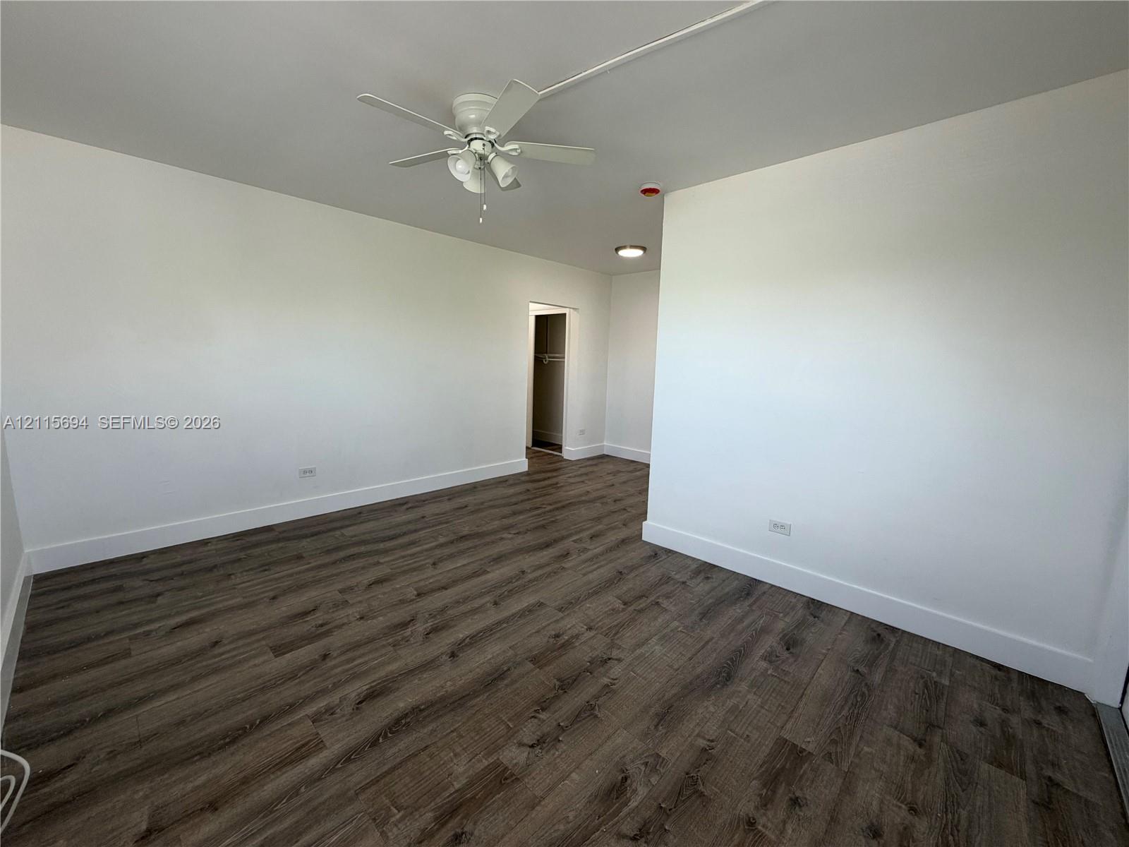 Room featuring wood-finish flooring, white walls, and a ceiling fan with integrated lighting