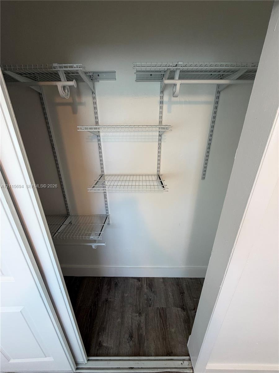Storage closet featuring white wire shelving, dual hanging rods, and wood-finish flooring