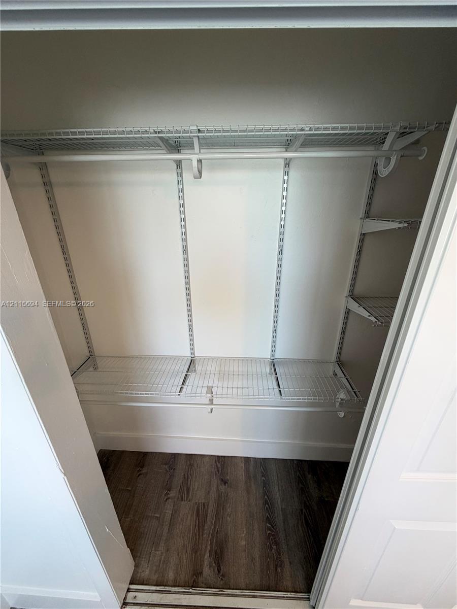 Storage space featuring white wire shelving, adjustable metal support tracks, and wood-finish flooring