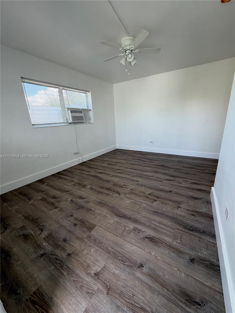 Interior room featuring wood-finish flooring, white walls, and a ceiling-mounted fan with integrated lighting