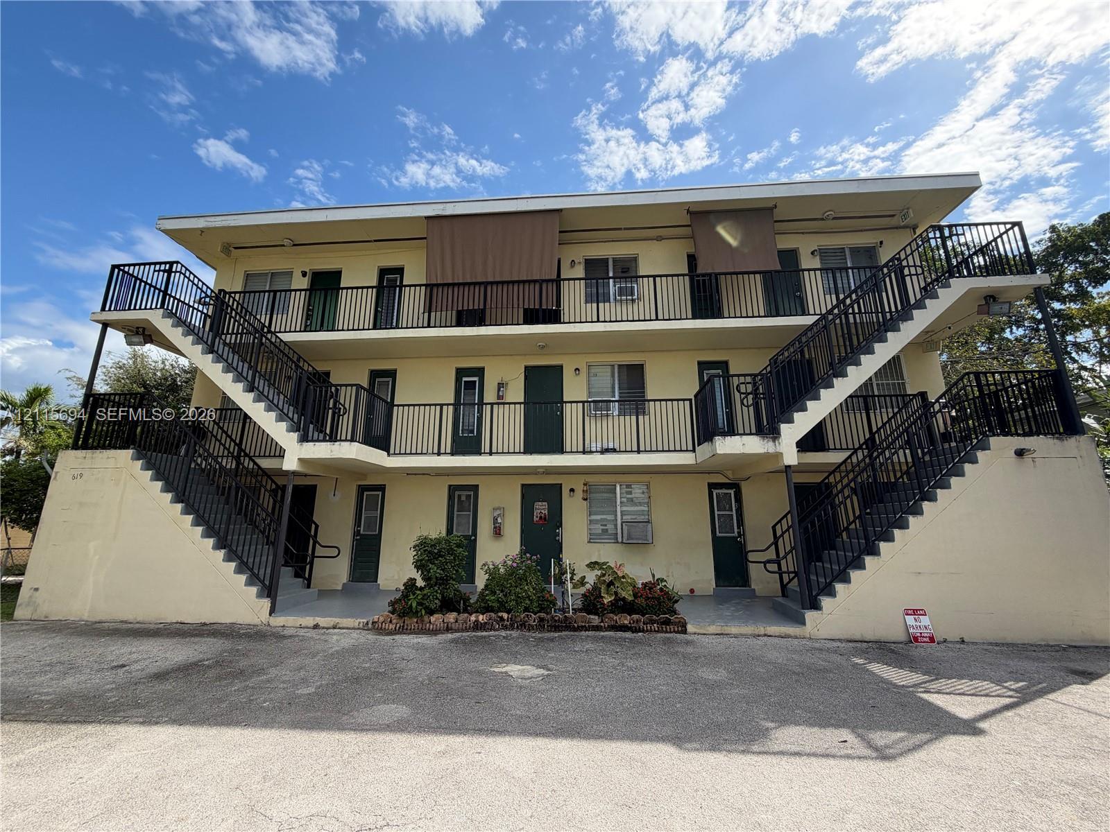 Three-story multi-unit exterior featuring concrete construction, dual symmetrical staircases, metal railings, and exterior walkways
