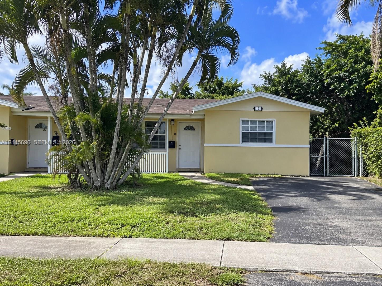 Single-story residence featuring a paved driveway, front lawn, mature palm trees, white exterior trim, and gated side access