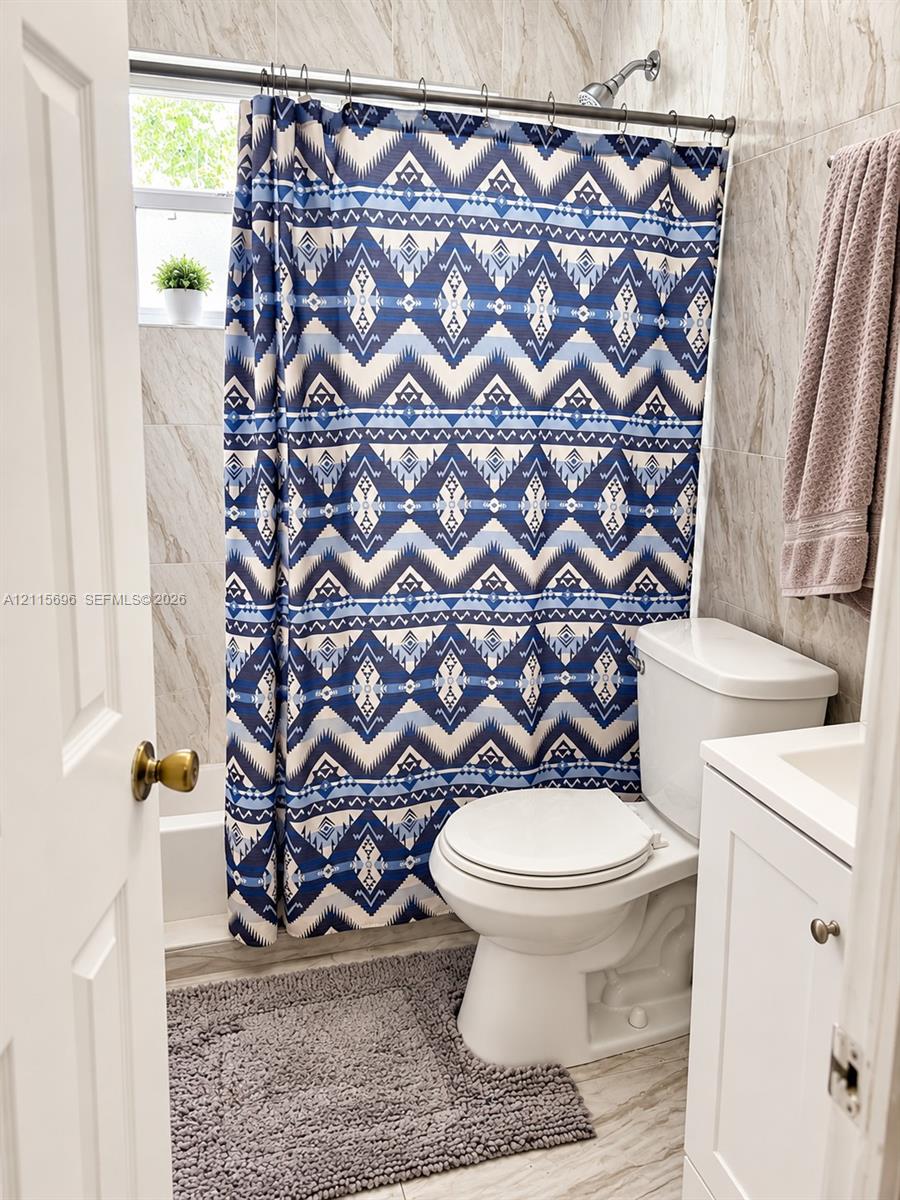 Bathroom featuring floor-to-ceiling neutral-toned tile, a white single-door vanity, a white porcelain toilet, and a combined tub and shower unit