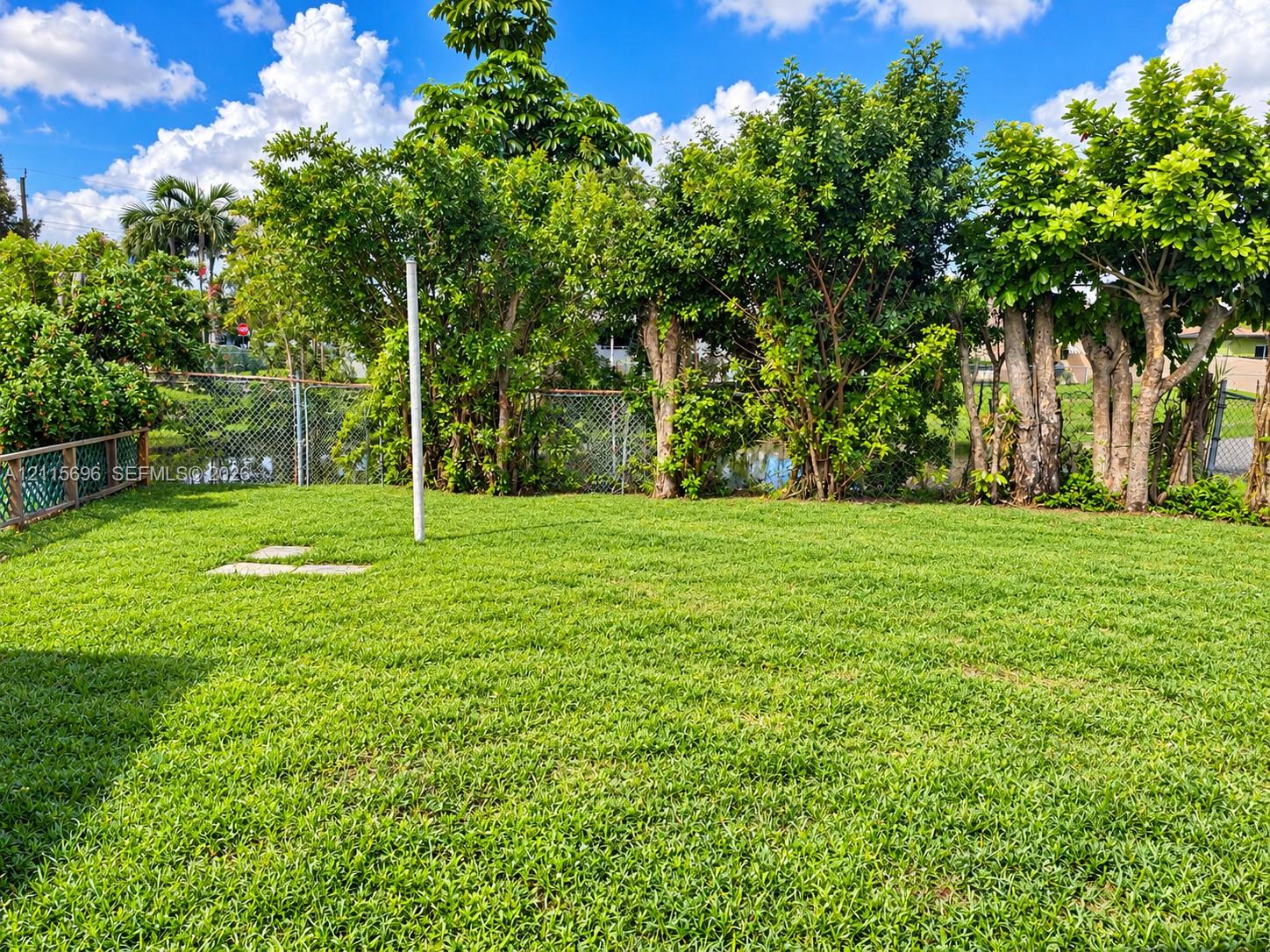 Expansive backyard featuring a level lawn, mature trees, chain-link fencing, and stone hardscaping elements