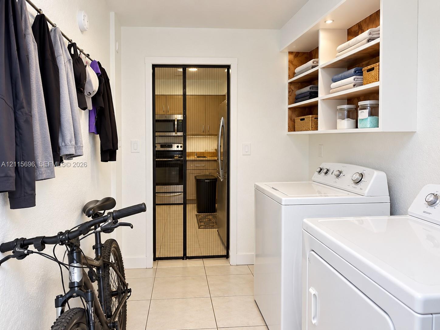 Laundry room featuring white tile flooring, built-in wall shelving with integrated recessed lighting, and a metal garment hanging rod