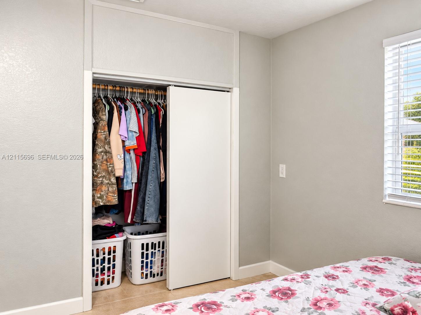 Built-in closet featuring floor-to-ceiling white sliding doors, neutral wall paint, and a horizontal window with white horizontal blinds
