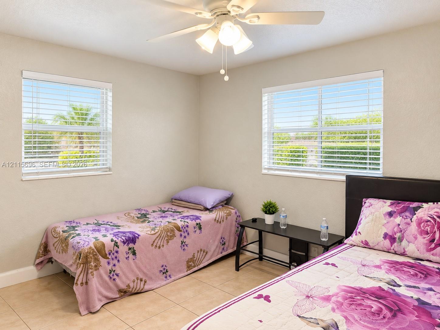 Neutral wall palette featuring dual windows with horizontal blinds, neutral tile flooring, and a ceiling-mounted light fixture with fan