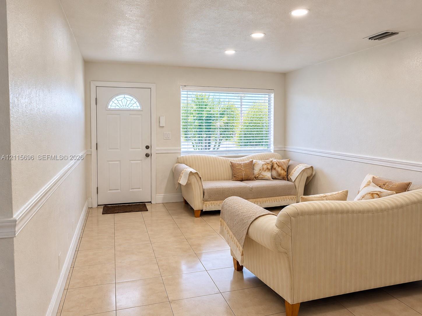 Neutral tile flooring, recessed lighting, white chair rail molding, and a front entry door featuring a decorative glass transom window