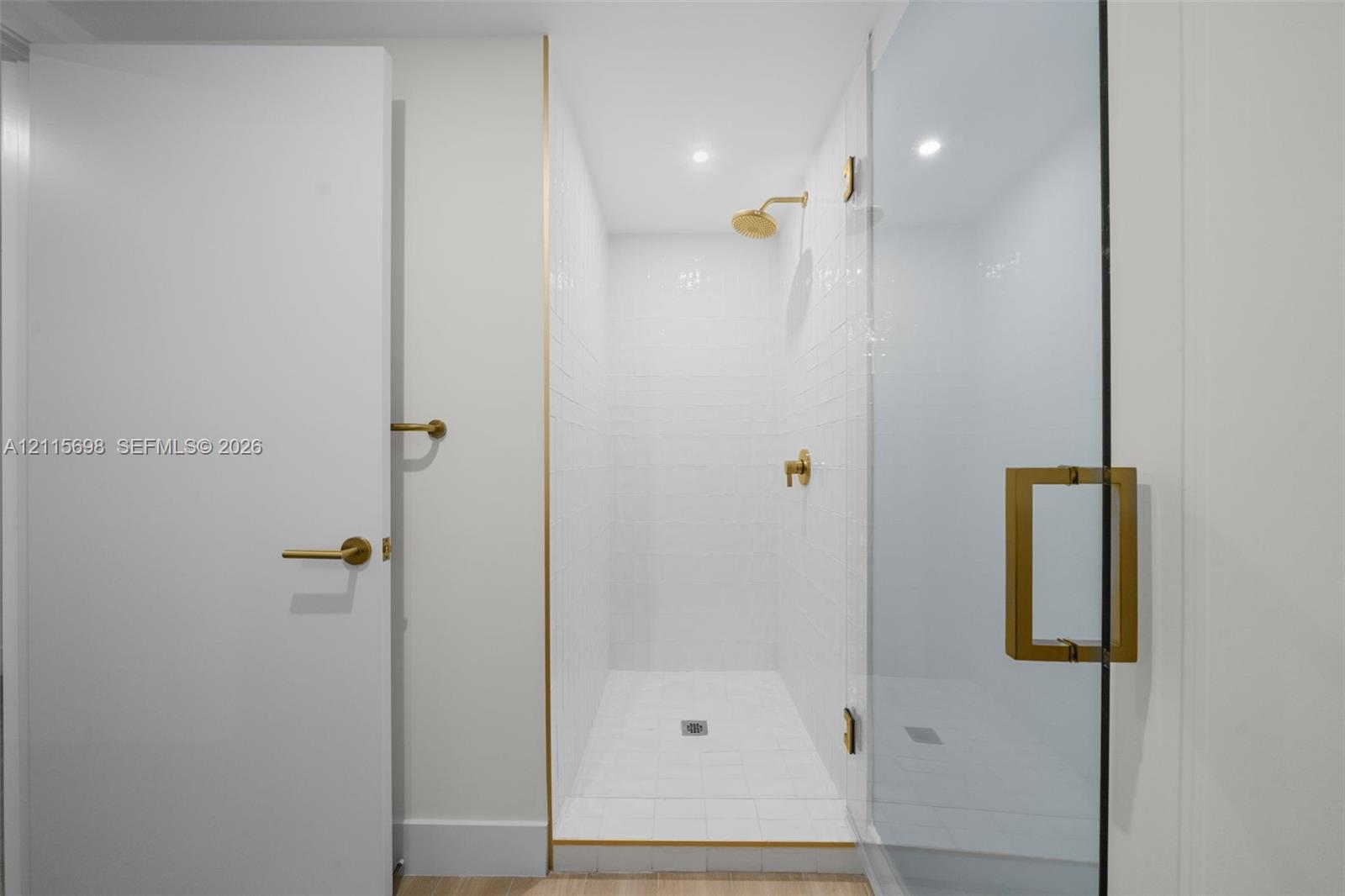 Guest bathroom with walk-in shower featuring white tiled walls and floor, clear glass enclosure, brass-finish fixtures, and gold-toned trim accents
