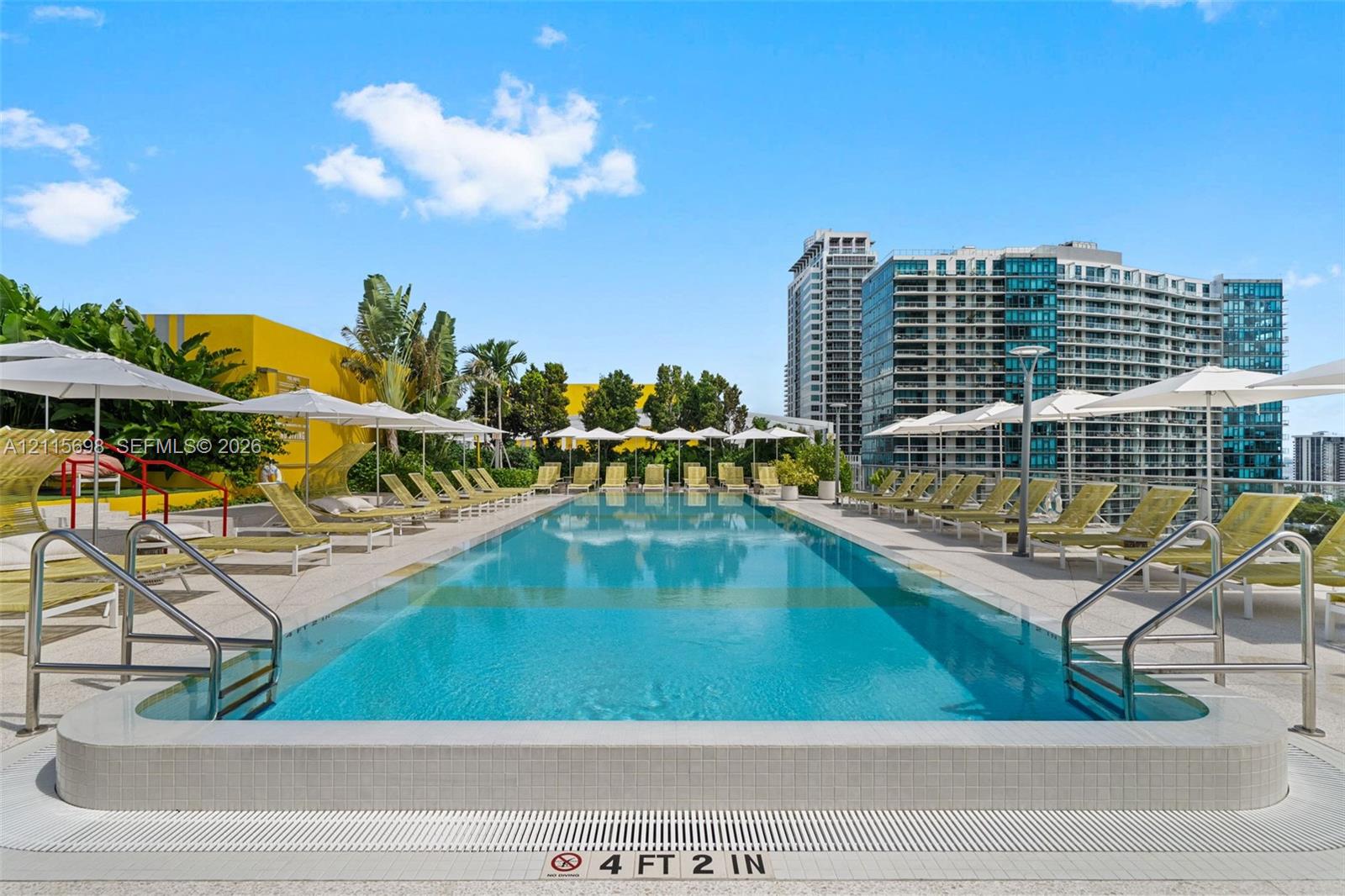 Rooftop lap pool featuring a tiled basin, aggregate pool deck, metal handrails, and a dedicated drainage perimeter