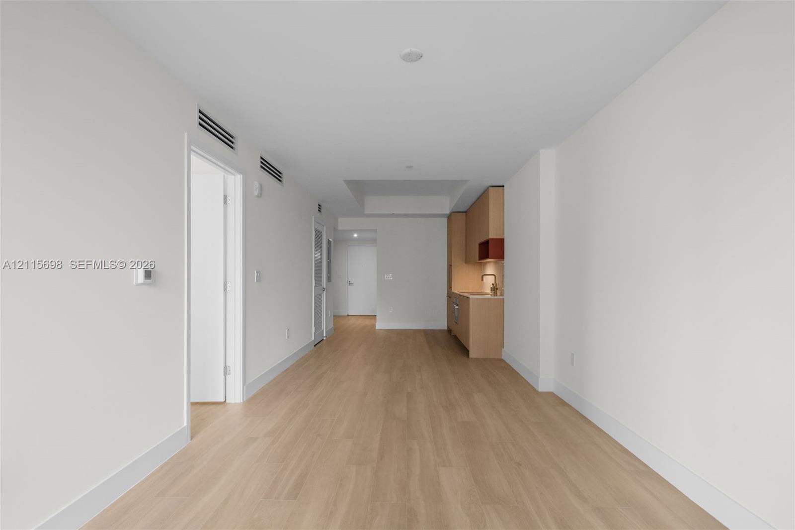 Light-toned wood-finish flooring, recessed ceiling lighting, and minimalist cabinetry with light-colored finish and metallic fixtures