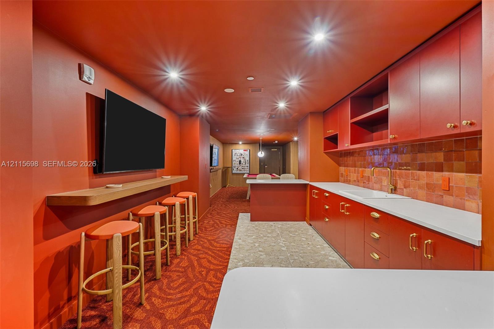 Building Amenity room with built-in cabinetry with brass-finish hardware, integrated sink, tile backsplash, countertop seating, and recessed ceiling lighting