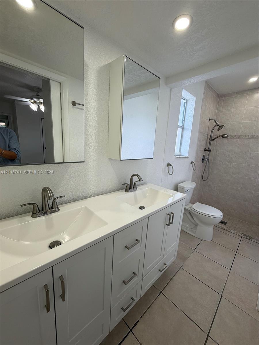 Dual-sink vanity with white cabinetry, light-toned solid surface countertop, rectangular under-mount sinks, mirrored medicine cabinets, and walk-in shower with adjustable showerhead