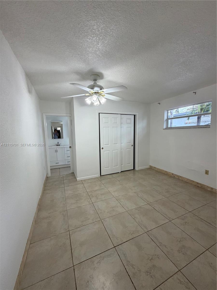 Room featuring neutral tile flooring, multi-panel bi-fold closet doors, a central ceiling fan with integrated lighting, and a single-pane horizontal window