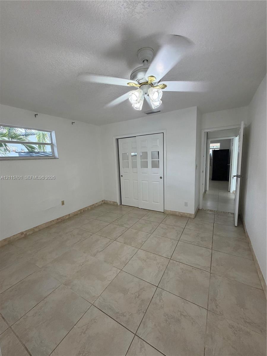 Room featuring large-format ceramic tile flooring, a multi-pane sliding closet door, and a ceiling fan with integrated lighting