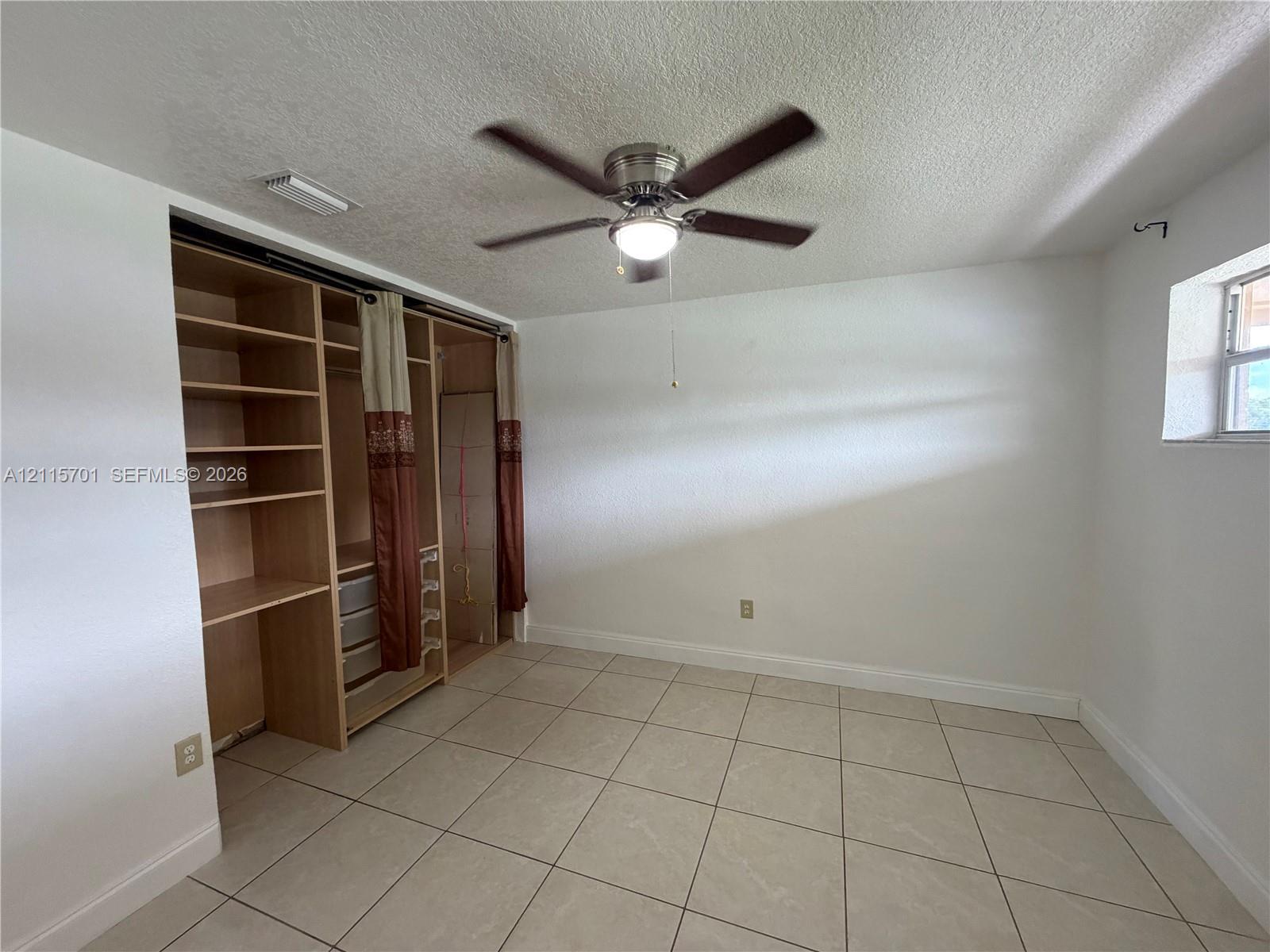 Interior room featuring large-format ceramic tile flooring, built-in wooden shelving unit with integrated storage, and a multi-blade ceiling fan with an attached light fixture