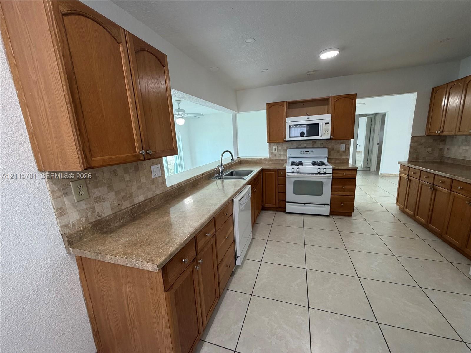 Kitchen featuring natural wood cabinetry, stone-finish countertops, tiled backsplash, integrated appliance suite, and ceramic tile flooring Kitchen featuring natural wood cabinetry, stone-finish countertops, tiled backsplash, integrated appliance suite, and ceramic tile flooring