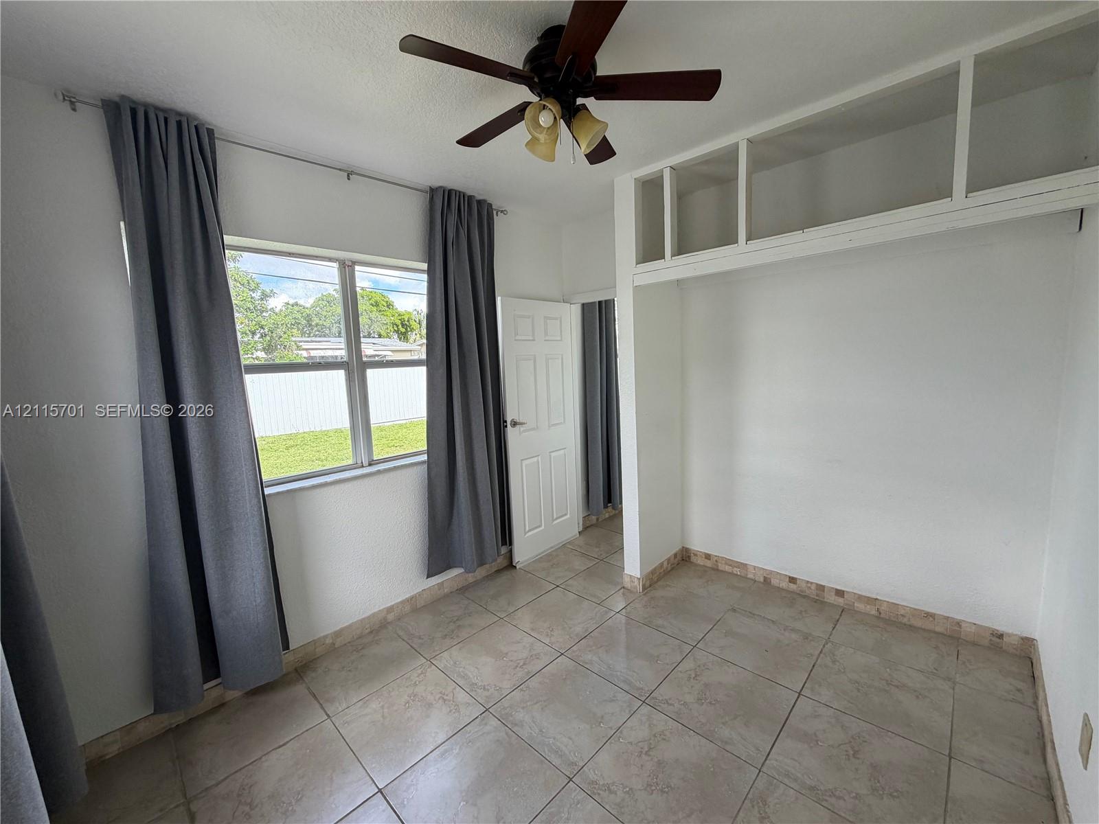 Room featuring neutral tile flooring, built-in overhead storage cabinetry, a multi-pane window, and a ceiling-mounted light fixture with a fan