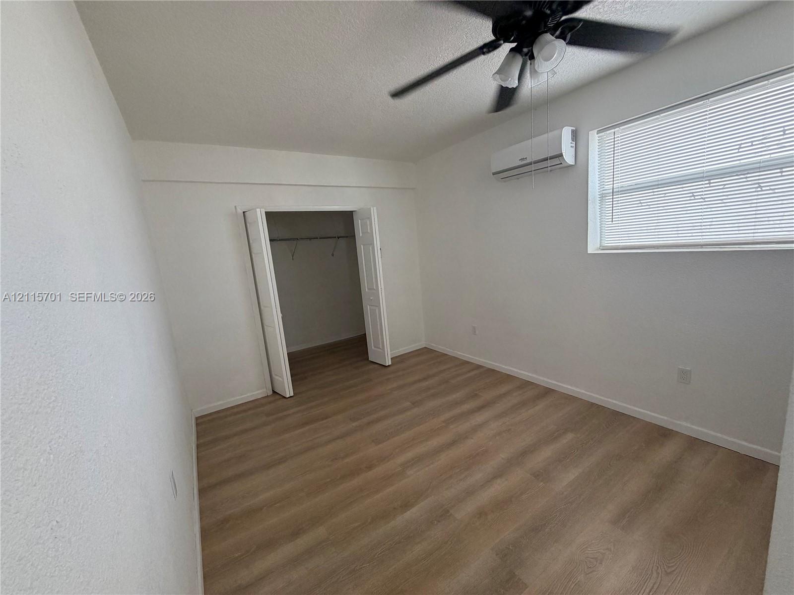 Interior room featuring wood-finish flooring, a wall-mounted ductless air conditioning unit, a ceiling fan with integrated lighting, and a closet with double-panel doors