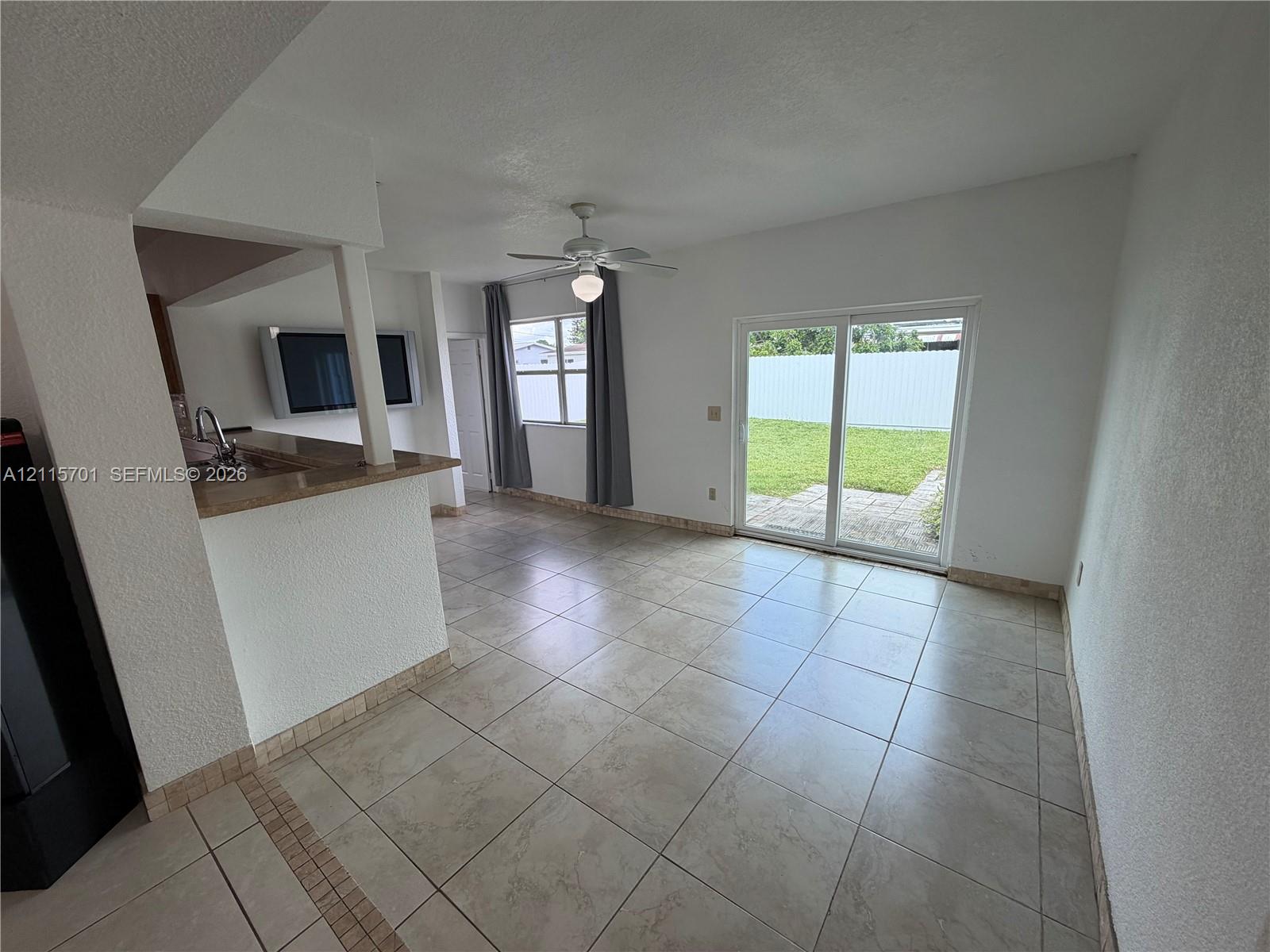 Tile flooring, kitchen breakfast bar with countertop, ceiling fan with light fixture, and sliding glass doors opening to a concrete patio and lawn Tile flooring, kitchen breakfast bar with countertop, ceiling fan with light fixture, and sliding glass doors opening to a concrete patio and lawn