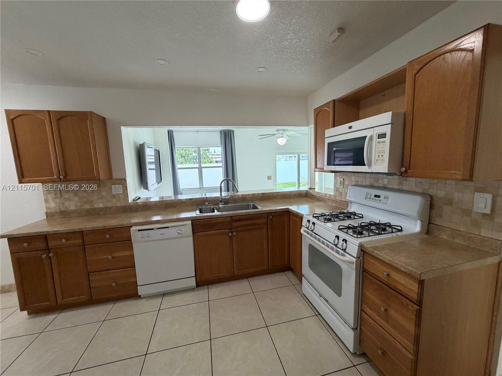 Kitchen featuring shaker-style wood cabinetry, stone-surface countertops, tile backsplash, dual-basin stainless steel sink, and recessed lighting