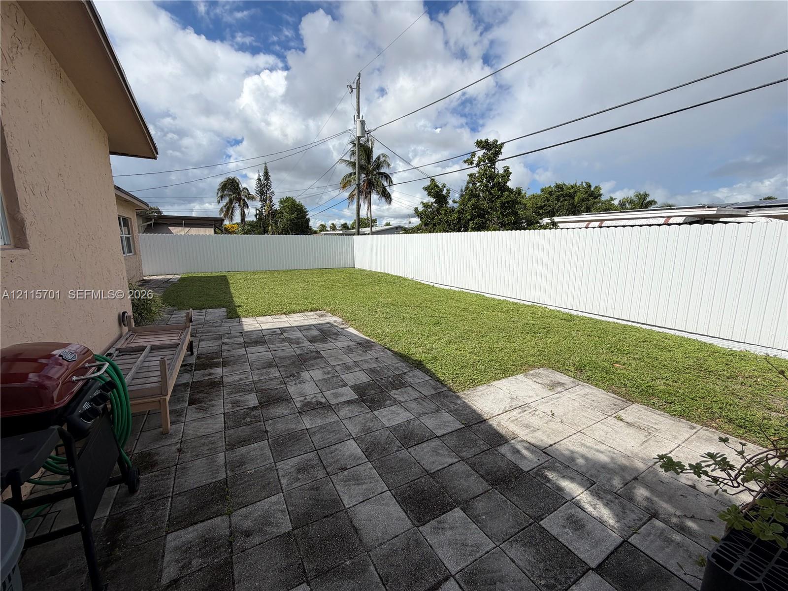 Backyard featuring a paved stone patio, a level lawn, and a white vinyl privacy fence