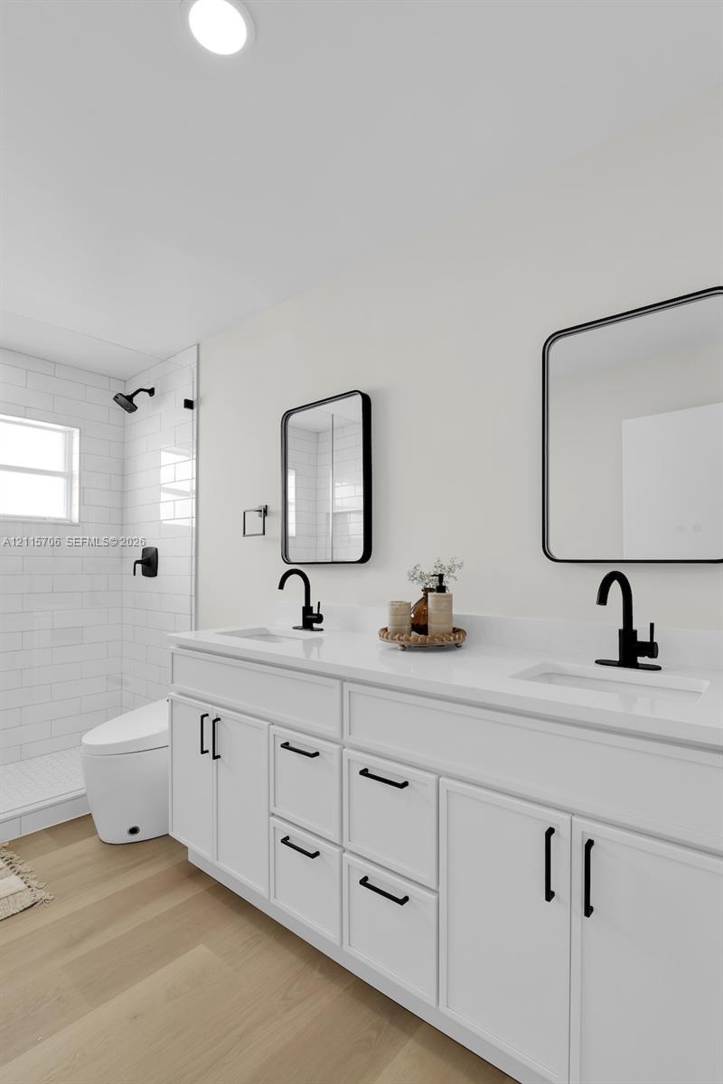 Dual-sink white vanity with quartz countertop, matte black fixtures, rectangular mirrors with black frames, and a tiled walk-in shower