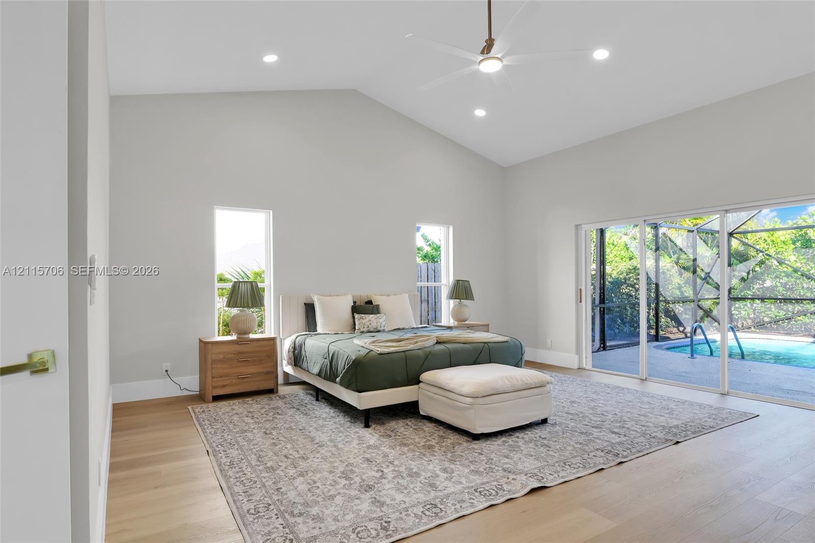 Vaulted ceiling featuring recessed lighting and a central ceiling fan, wood-finish flooring, and sliding glass doors with direct access to a screened-in swimming pool