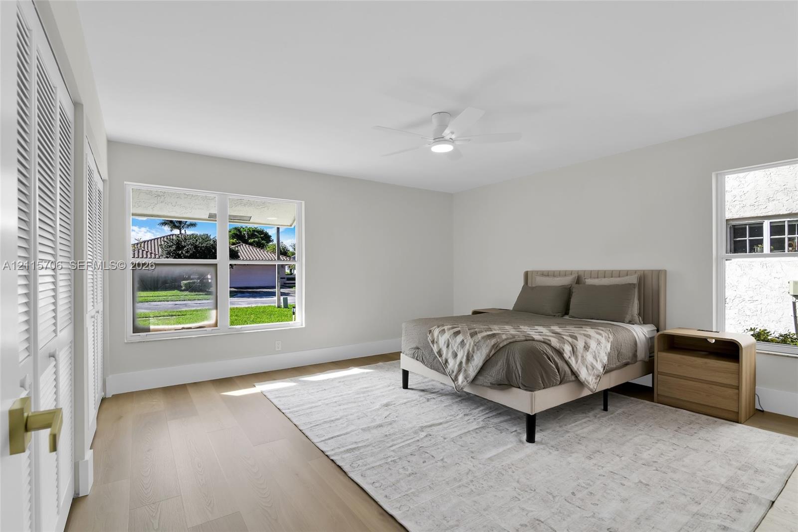 Neutral-toned interior featuring wood-finish flooring, dual windows, louvered closet doors, and a ceiling-mounted light fixture
