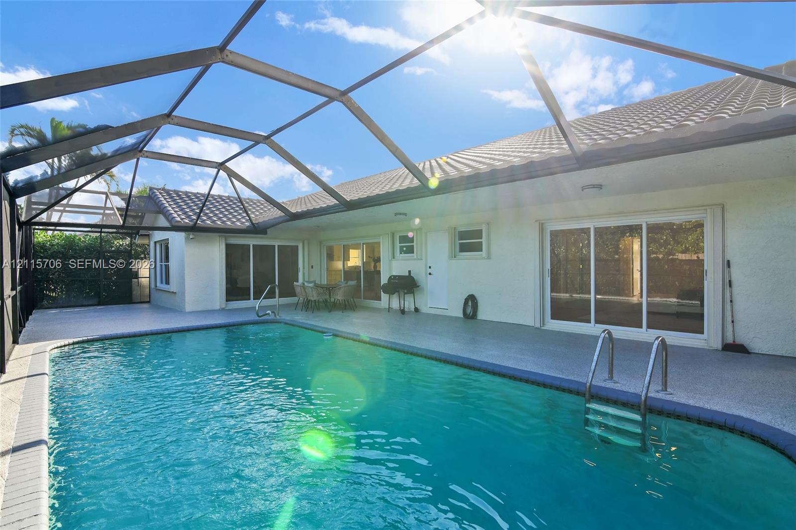 Screened-in pool deck featuring a tiled-finish swimming pool, paved patio, and metal pool cage