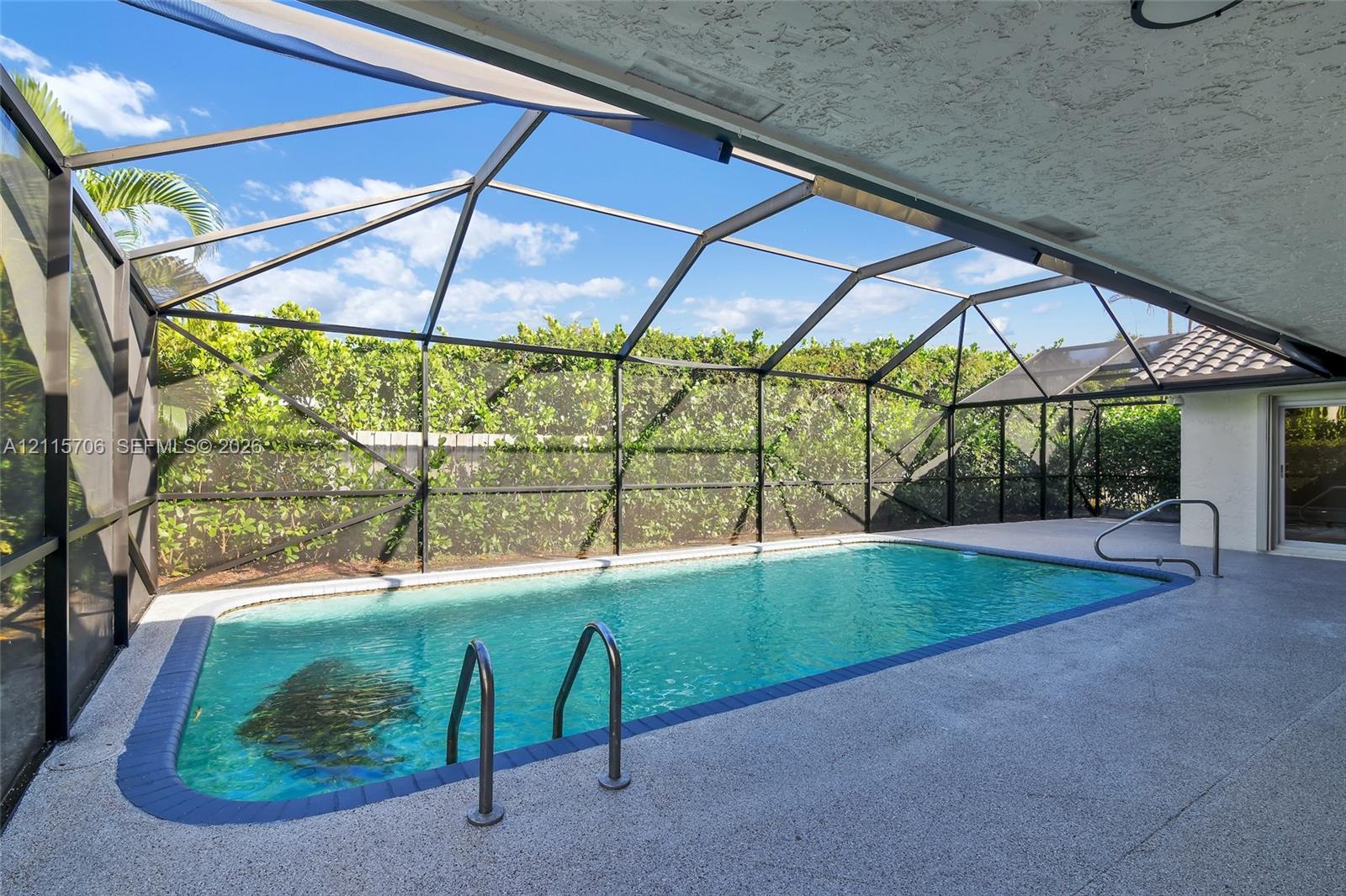 Screen-enclosed swimming pool featuring a textured concrete deck, a tiled perimeter, and metal handrails