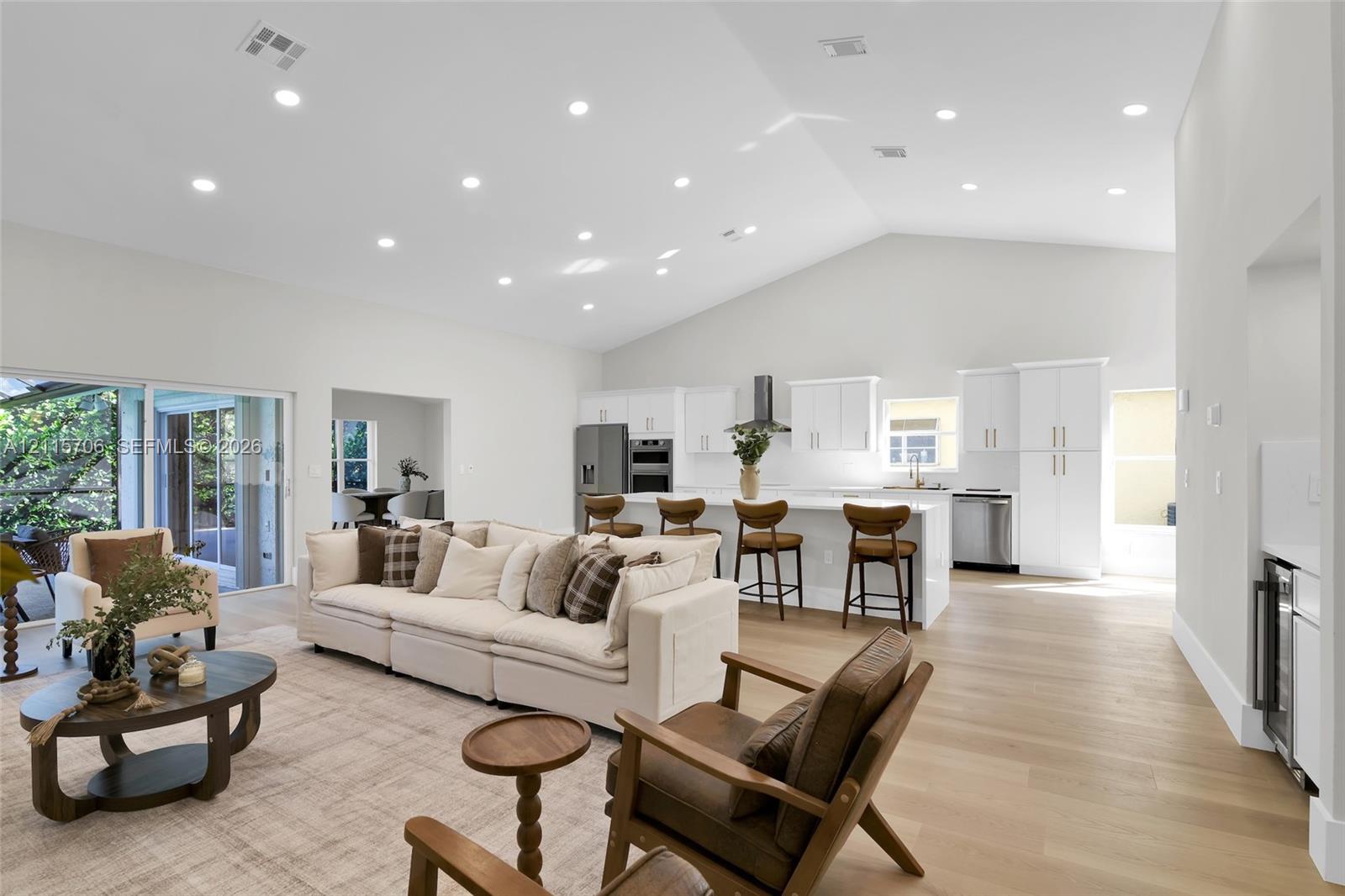 Open-concept interior featuring vaulted ceilings, recessed lighting, wood-finish flooring, white cabinetry, and a kitchen island with stone-finish countertops