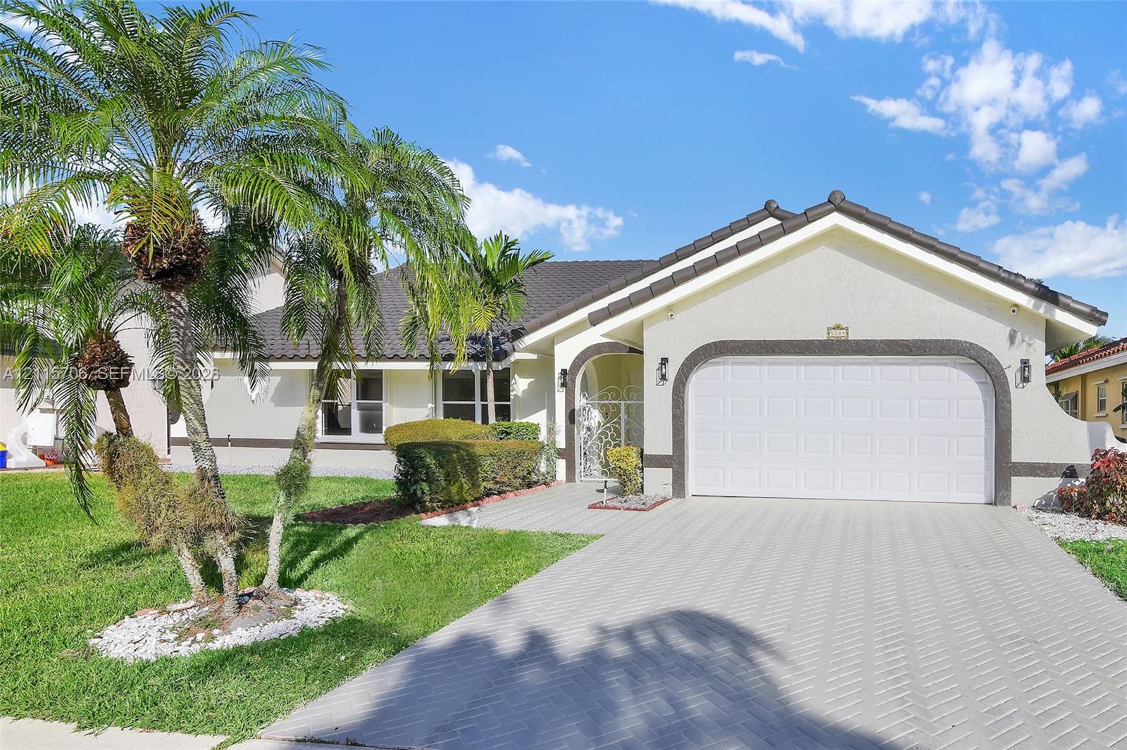 Stucco exterior featuring a tiled roof, arched entryway with ornamental iron gate, two-car garage with arched trim, and paved driveway