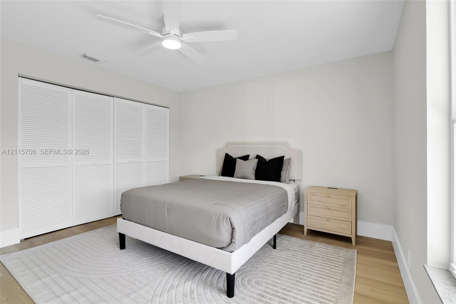 Bedroom featuring wood-finish flooring, white louvered-style closet doors, and a ceiling-mounted light fixture with a fan
