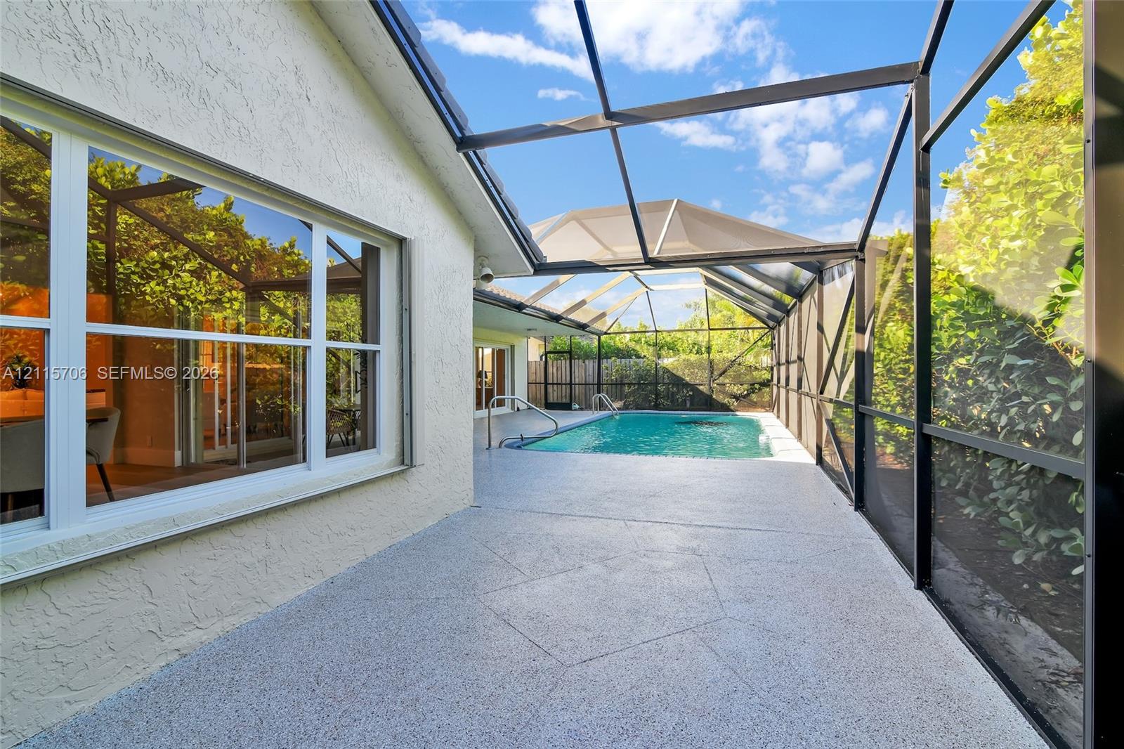 Screened-in patio featuring a swimming pool, textured concrete deck, metal frame enclosure, and exterior light-colored masonry finish