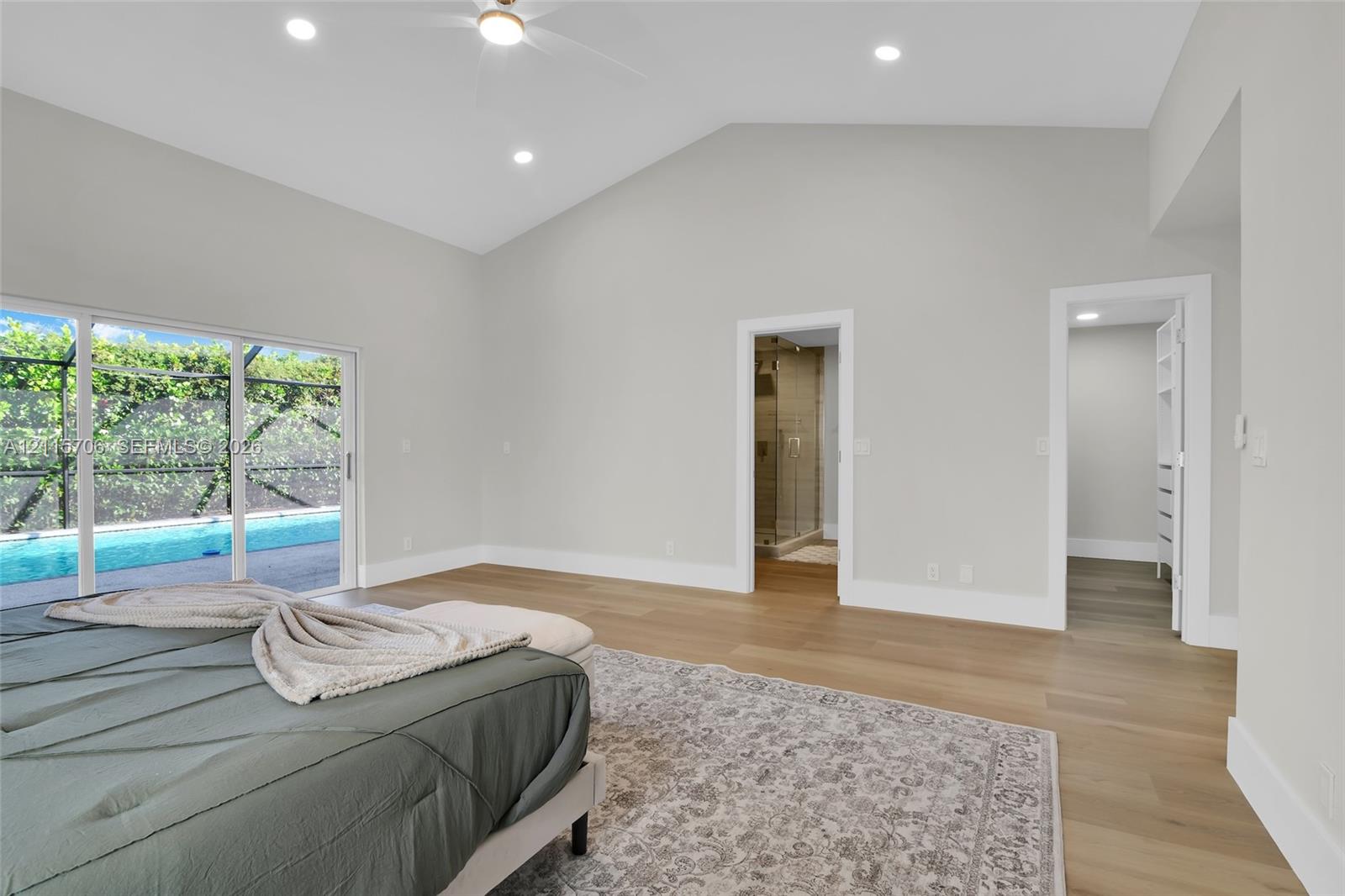 Vaulted ceilings, wood-finish flooring, recessed lighting, and sliding glass doors with access to a screened-in pool enclosure