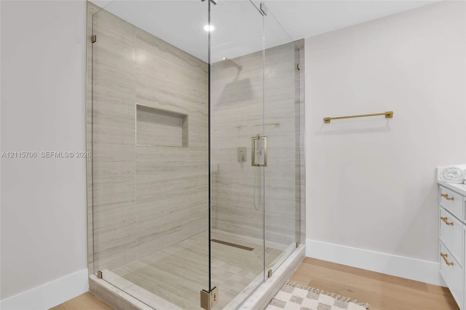 Walk-in shower featuring a frameless glass enclosure, horizontal stone-tile wall surround, built-in recessed wall niche, linear floor drain, and brushed gold-tone fixtures