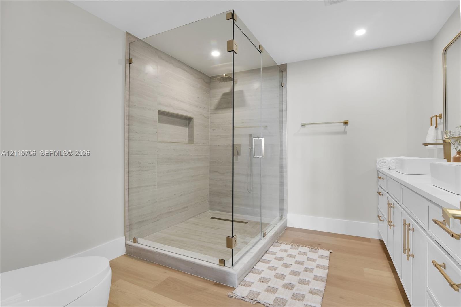 Walk-in shower featuring a frameless glass enclosure, floor-to-ceiling stone-style wall tile, and an integrated wall niche