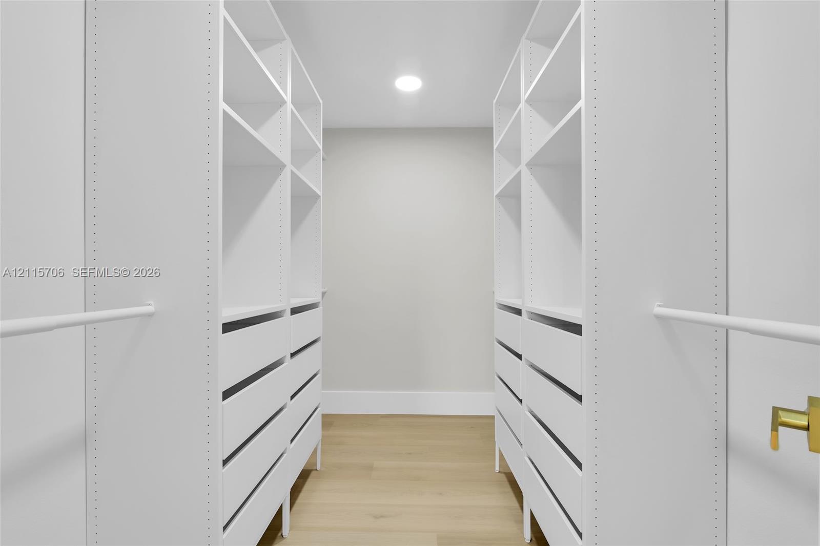 Built-in custom cabinetry featuring white shelving, multiple integrated storage drawers, and white hanging rods, complemented by wood-finish flooring and recessed ceiling lighting