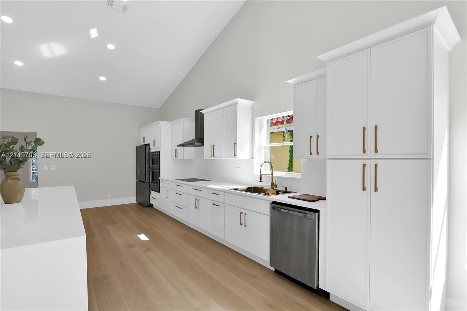 Kitchen featuring vaulted ceilings, shaker-style cabinetry with brass-finish hardware, quartz countertops, wood-finish flooring, and stainless steel appliances