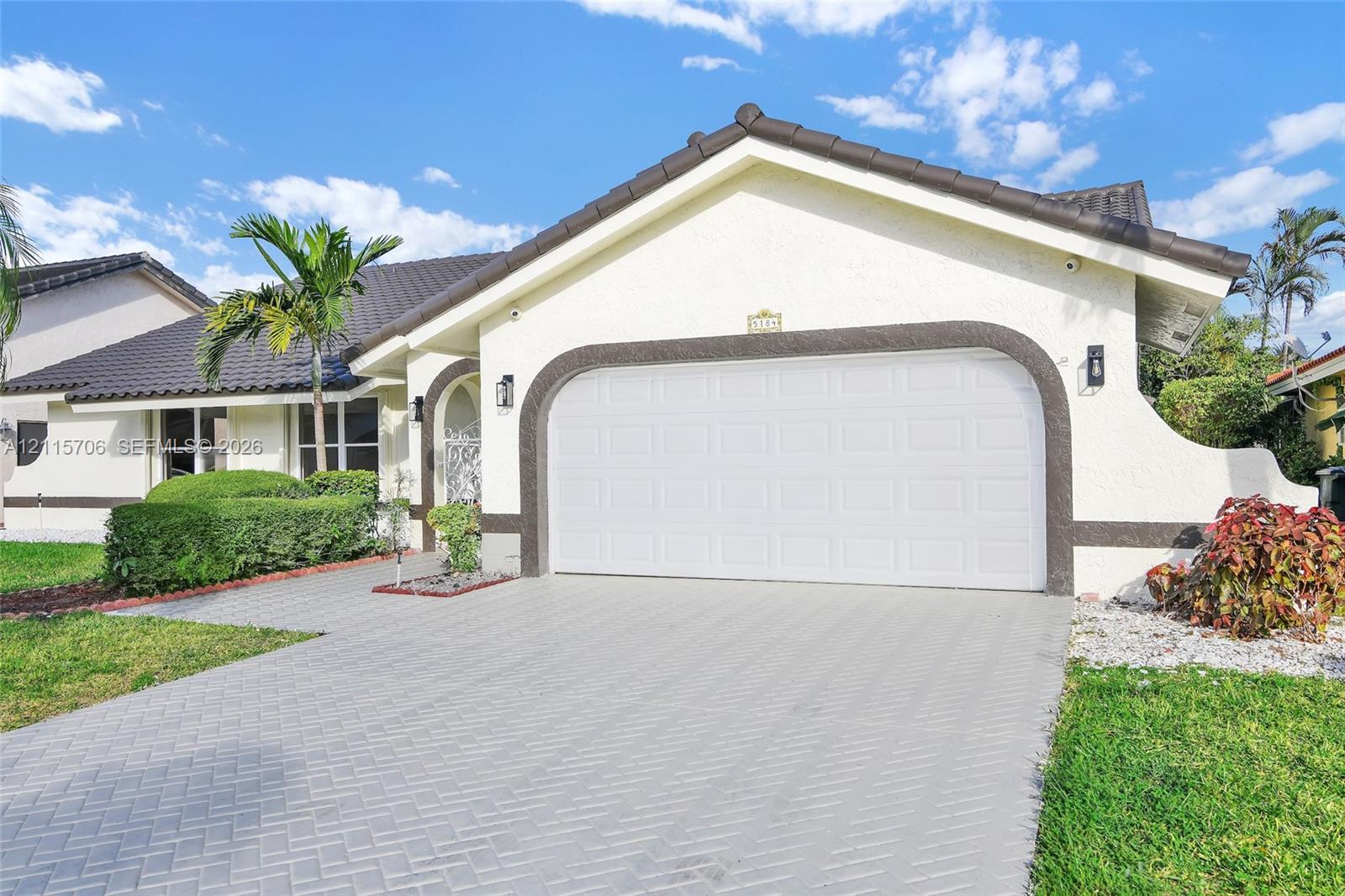 Stucco exterior with decorative arched trim, herringbone-patterned paver driveway, two-car garage, and tiled roof