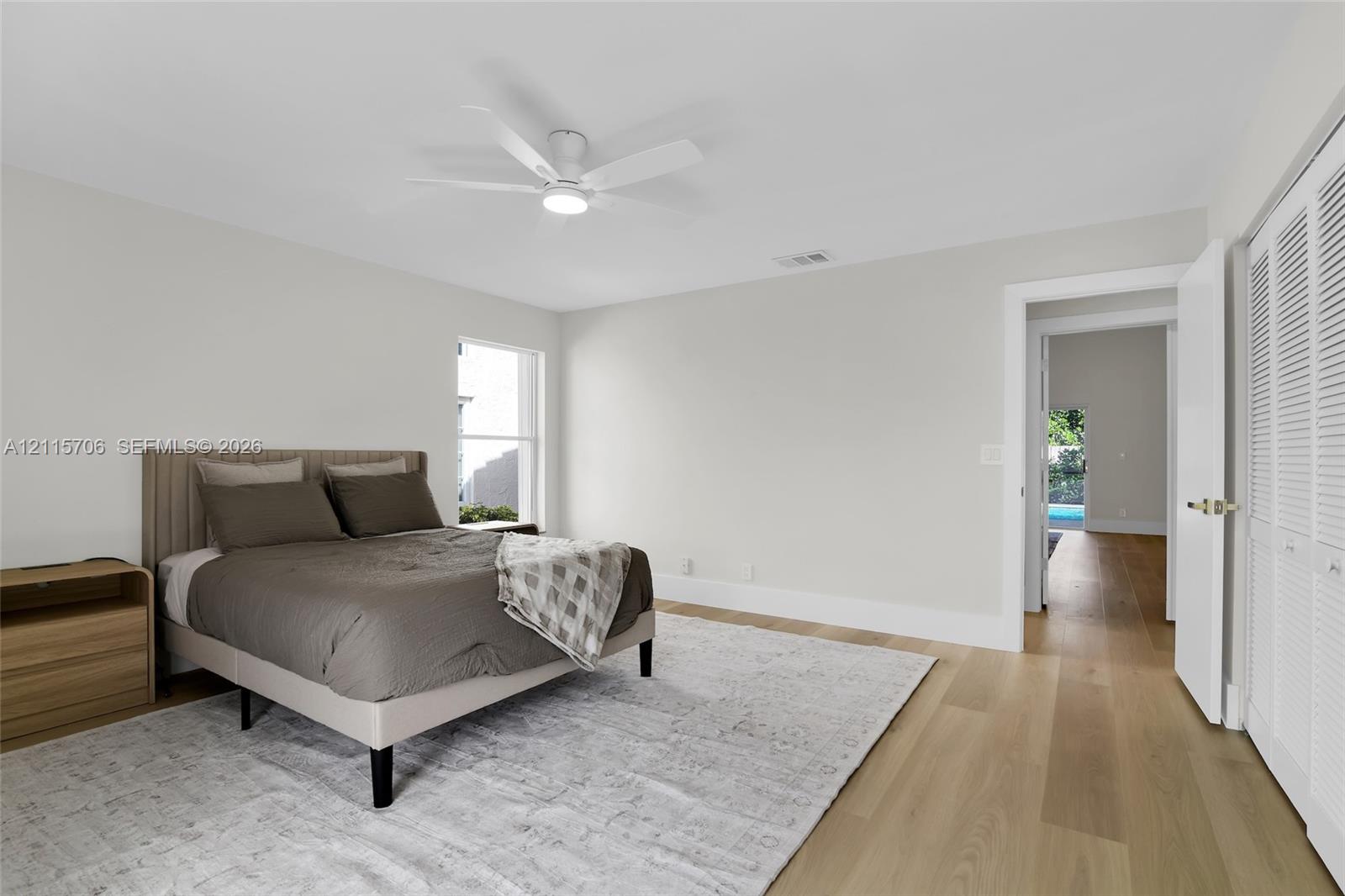 Neutral-toned room featuring wood-finish flooring, a white ceiling fan with integrated lighting, and louvered closet doors