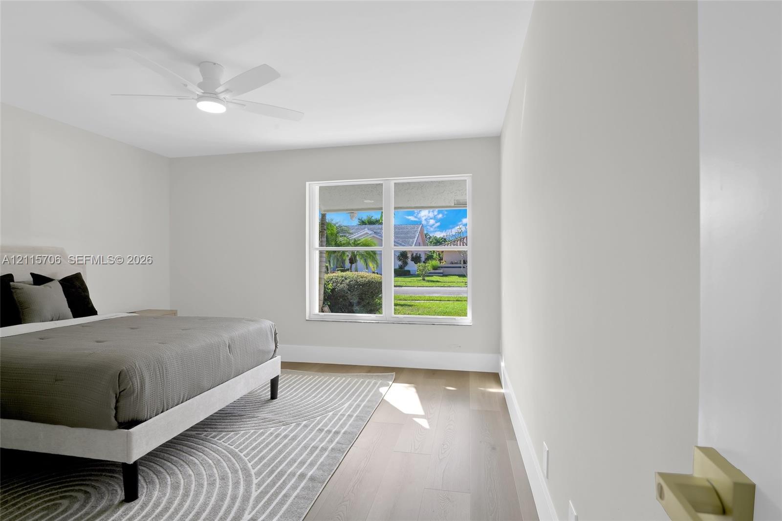 Neutral-toned interior featuring wood-finish flooring, a white ceiling fan with integrated lighting, and a large dual-pane window