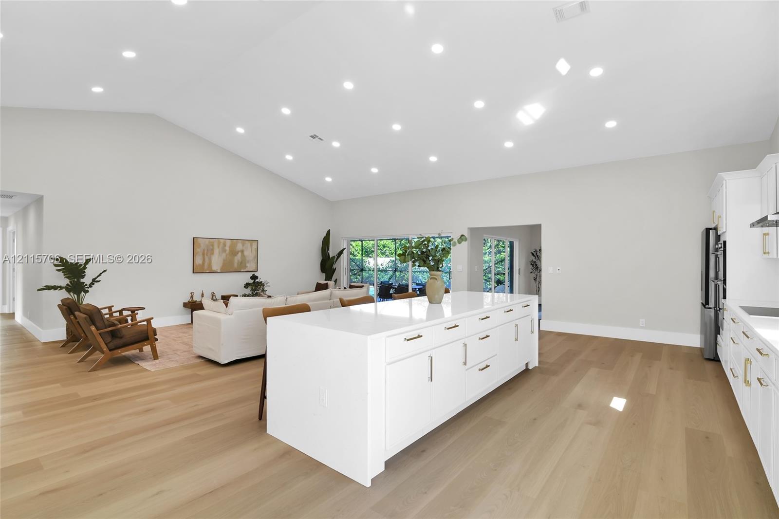 Open-concept interior featuring vaulted ceilings, recessed lighting, wood-finish flooring, a white kitchen island with cabinetry, and large sliding glass doors